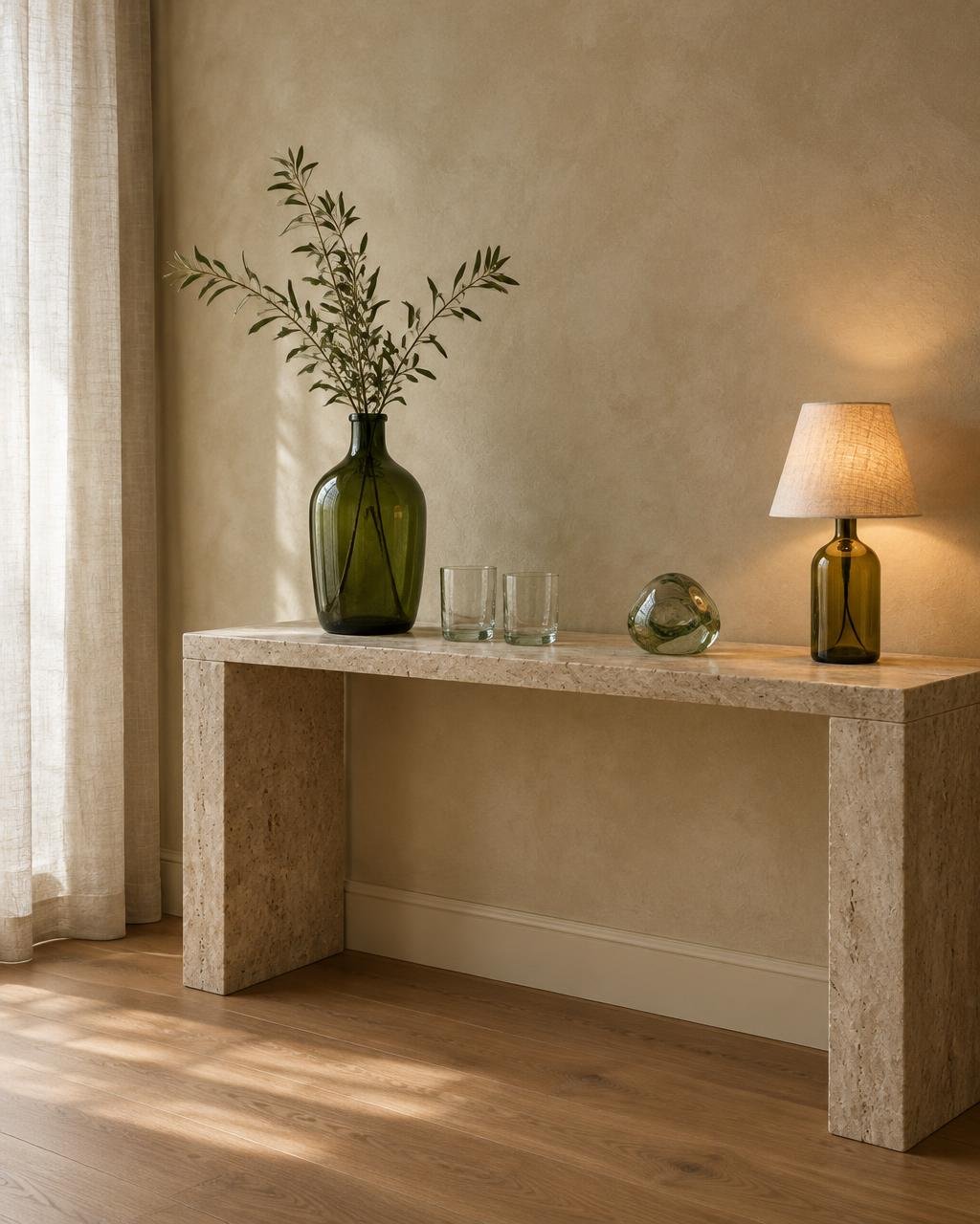 Upcycled green bottle-glass vase, tumblers and a bottle lamp styled on a travertine console in soft daylight